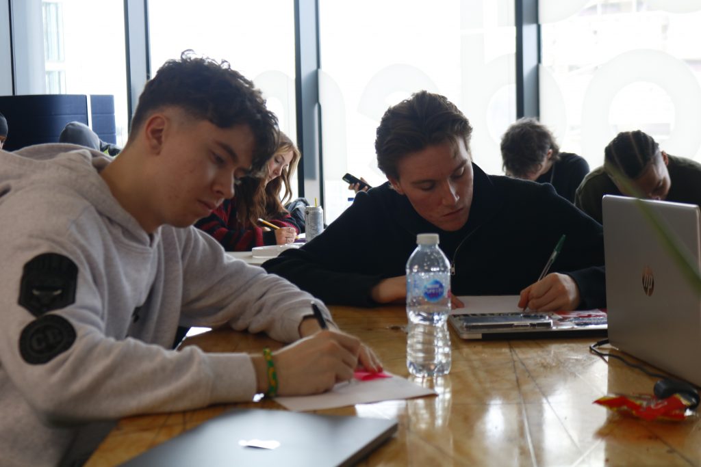 Students sitting at a desk with a pen and paper in class at unique media school. 