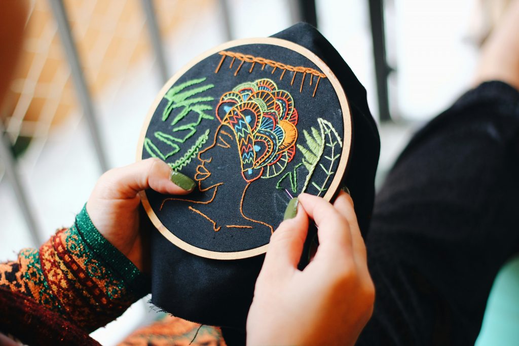 Women hand-embroidering a colourful design full of different stitch types. 