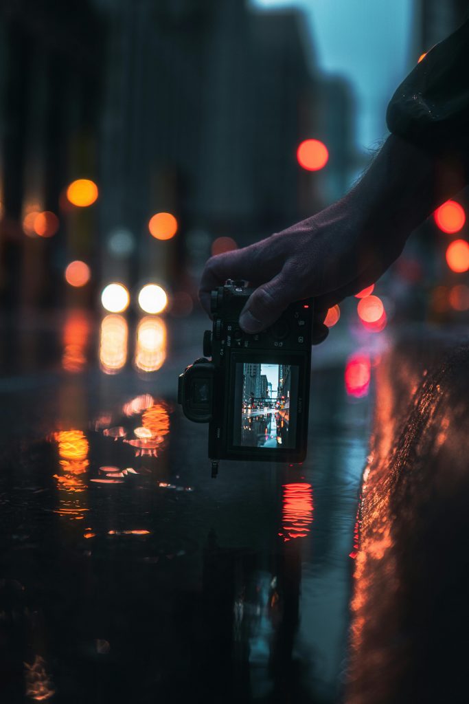 A digital camera capturing a colourful scene of city lights reflecting against a puddle of water.