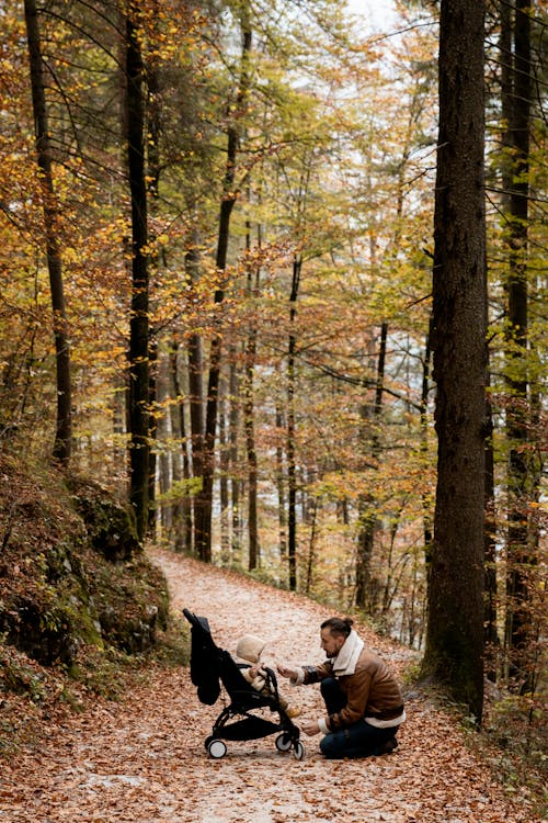 "Man kneeling down to feed a baby in a luxury Bugaboo stroller"