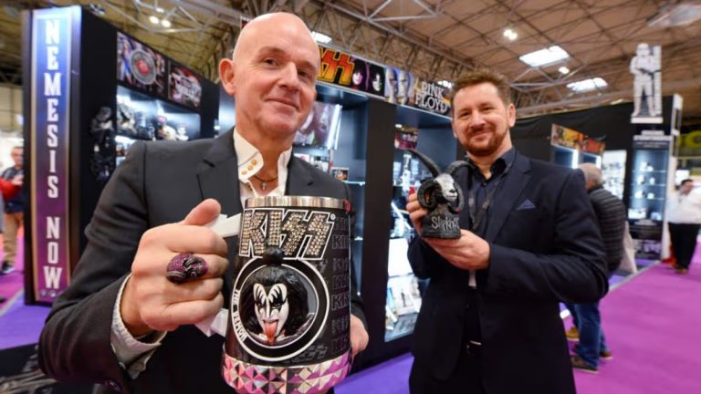 Two men in suits standing in front of a Nemesis Now display stall. One holds a KISS tankard, while the other holds a Slipknot tankard.