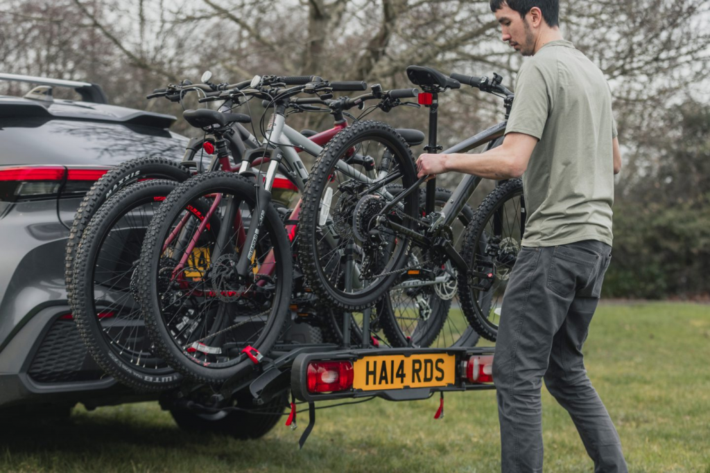 A man is placing 4 bikes on a tow-bar bike rack attached to a car.